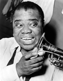 Louis Armstrong looks at his trumpet with a big smile on his face.