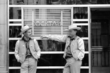 2 men in western wear stanidng outside a bar with a neon sign for cocktails
