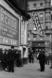 Men lounging in front of the arcade, Butte, Montana. Sign shows Blatz is on tap.