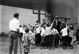 large group of children playing basketball while a school teacher with a cane looks on.