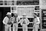 Four cowboys dress alike in front of bar, Billings, Montana. Neon lounge sign hangs in the window