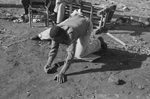 A man is kneeled over shooting marbles. The game has rules similar to golf.