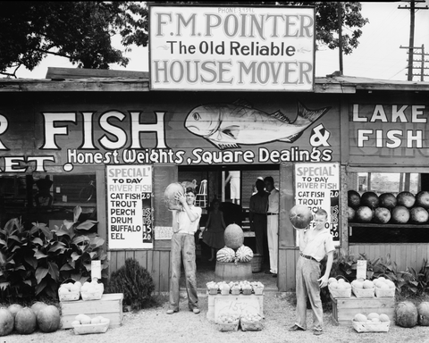 Childern holding watermelons. Other signs mention f.m. pointer the old reliable house mover and today's fish special. 