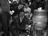 A keg of beer was opened at the scrap salvage campaign in Butte Montana. A young man pours beer from a keg while others wait cup in hand.